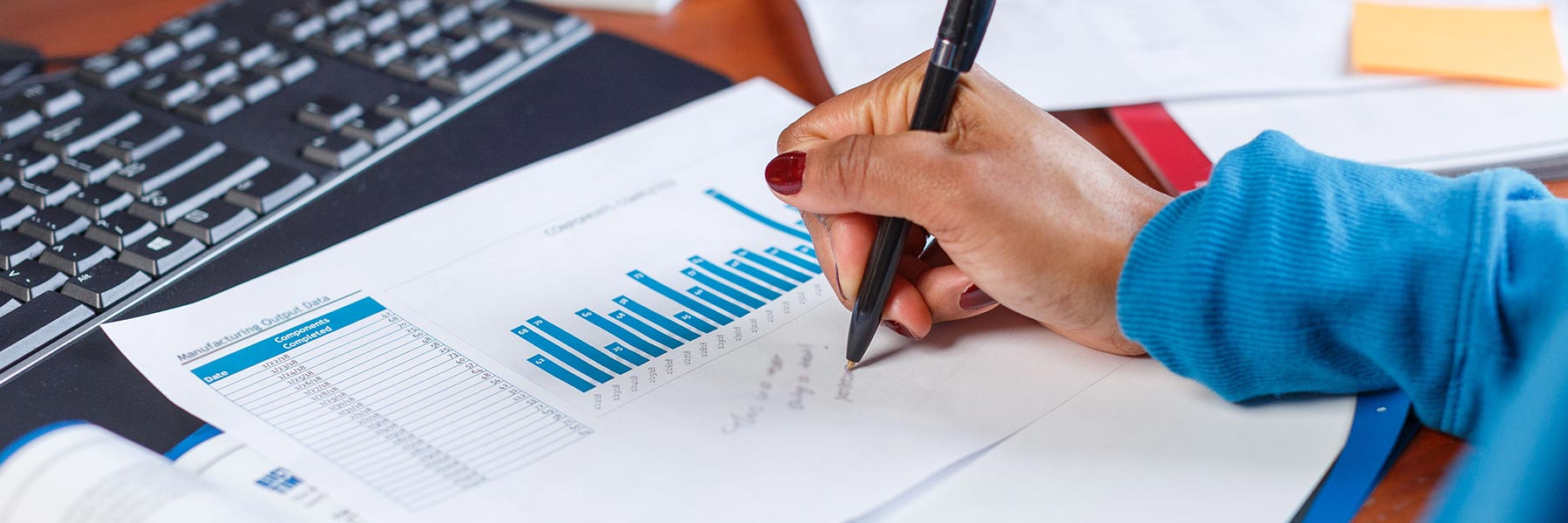 A close-up of a hand that uses a pen to write beside a chart