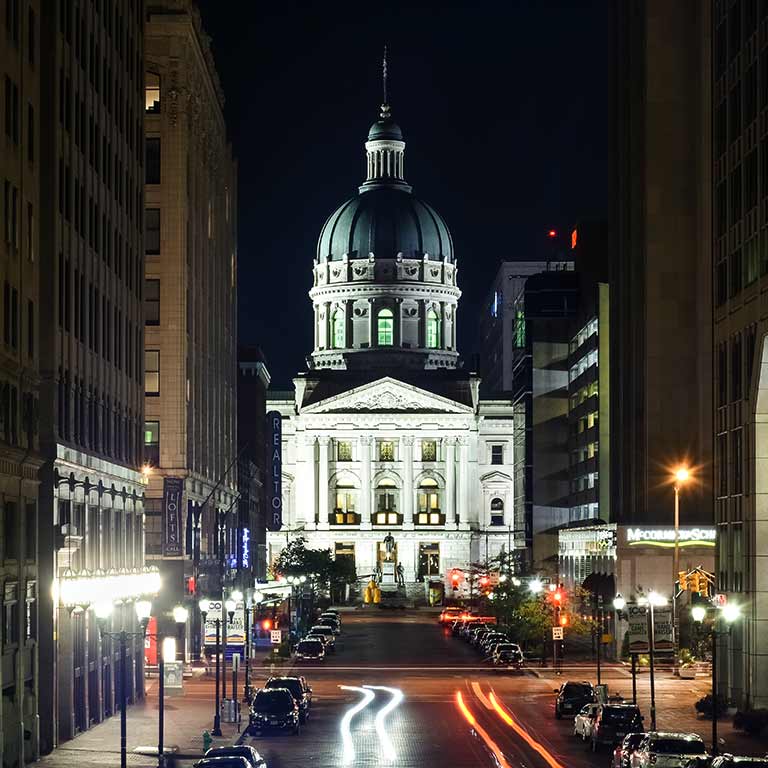 A city street that leads to a capitol building and is lined with street lights