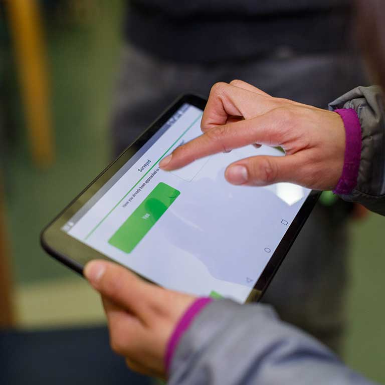 Close-up photo of a woman's hands holding a tablet filling out a survey